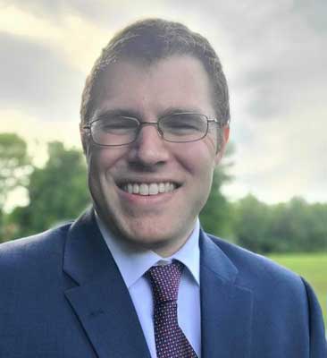 Chest-up outdoor portrait of Ian McCrum in a blue sports coat and read tie