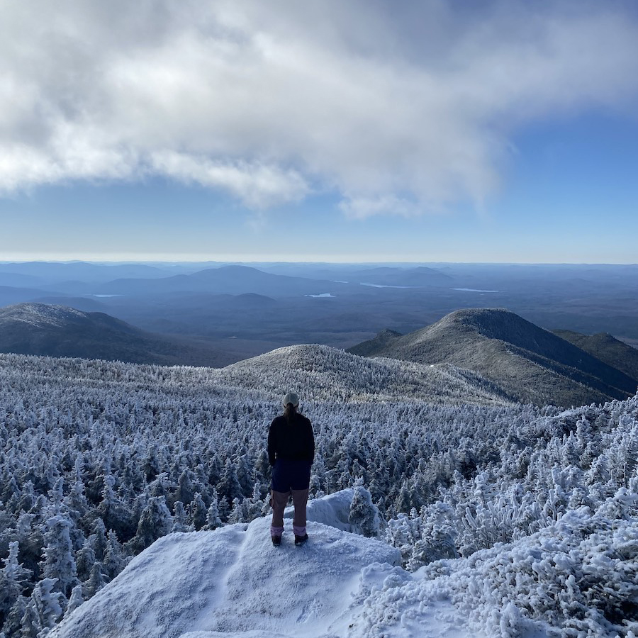 A person standing on top of a mountain looking out over other mountains that are covered in a bright layer of snow