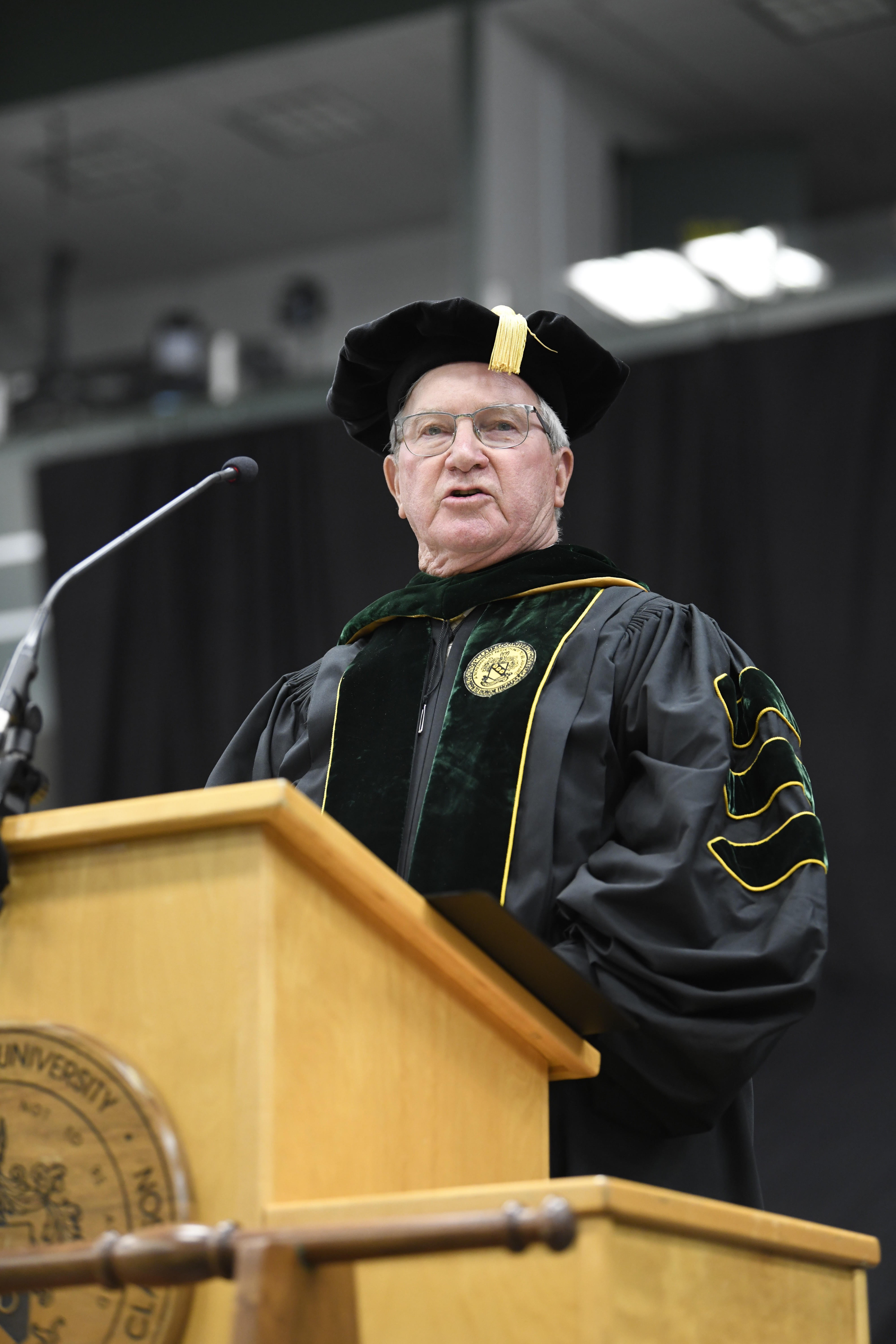 Hunter Peckham stands at a podium in regalia as he speaks to an audience not pictured.