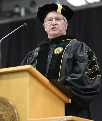 Hunter Peckham stands at a podium in regalia as he speaks to an audience not pictured