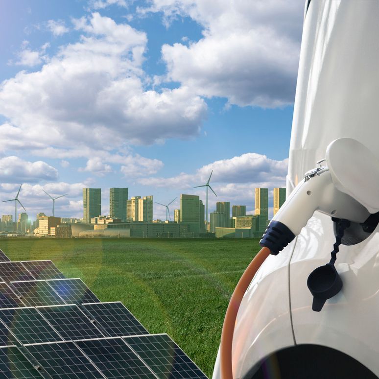 A white electric vehicle charges in front of a solar array and faraway city skyline.