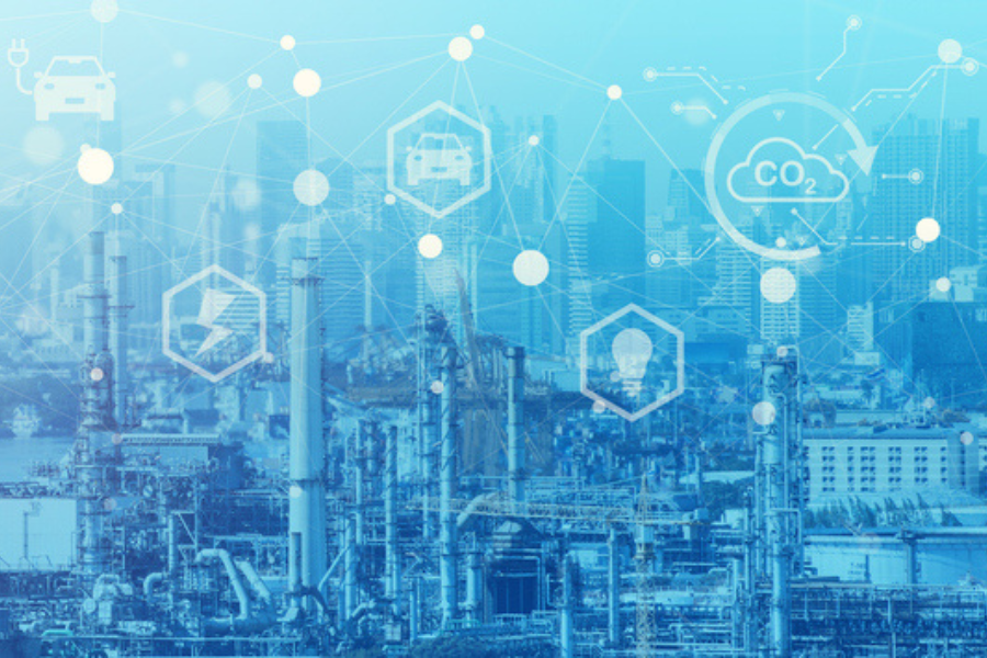 An industrial facility with interconnected icons overlaid, representing electric vehicles, renewable energy, light bulbs, and CO2 reduction, all against a blue-toned cityscape background. The image emphasizes industrial efforts to reduce carbon emissions through technology.