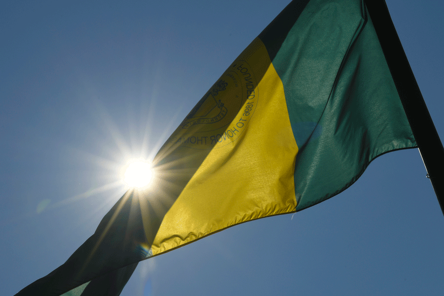 A green and yellow flag blows in the sun that reads Clarkson Honors