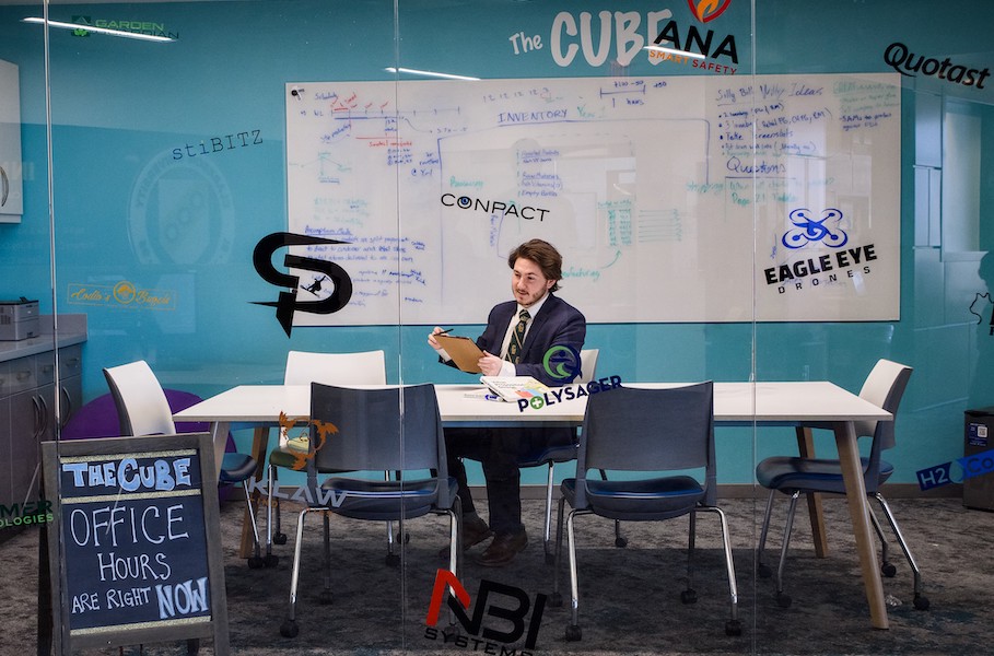 A man at Clarkson University sits inside a glass-walled room named the Cube while preparing business plan information using a clipboard.