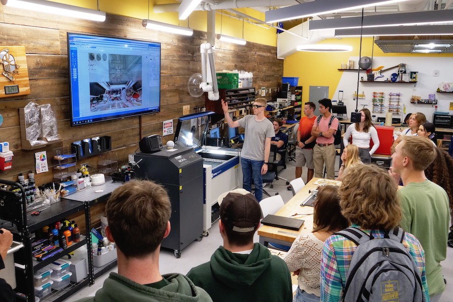 A group of students stand while listening to a presentation in the Dorf Makerspace.