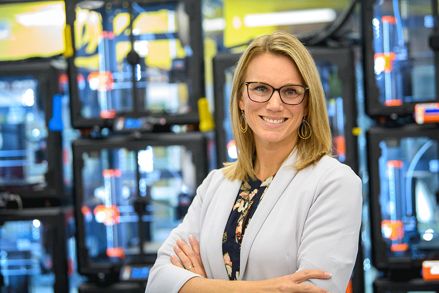 Ignite director Ashley Sweeney poses with arms crossed in front of a wall of 3D printers