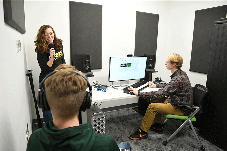 Three Clarkson students test our Clarkson's media production center. One student uses a microphone, while another works on a computer and keyboard, and a third wears headphones.