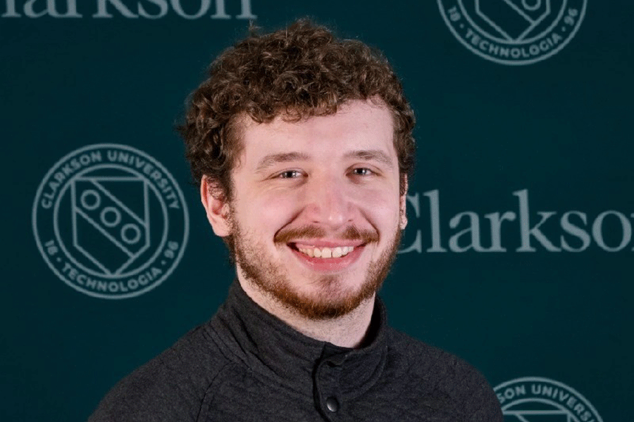 Clarkson Ignite program coordinator Demetrius Boone smiles for a headshot in front of a Clarkson logo step and repeat banner