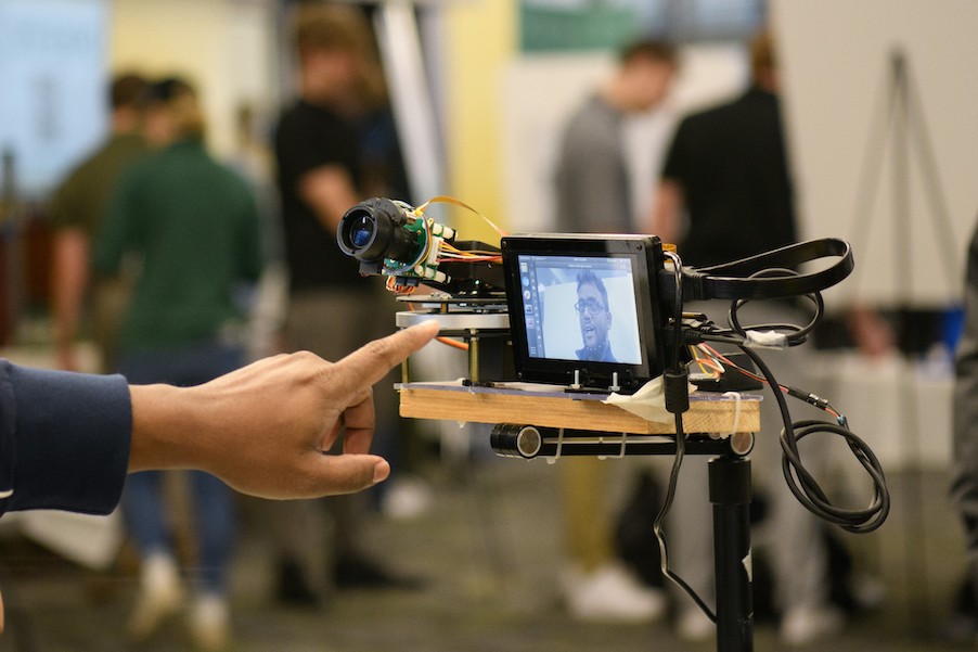 A male finger points at a small computer screen displaying a picture of a man’s face captured by a connected camera.