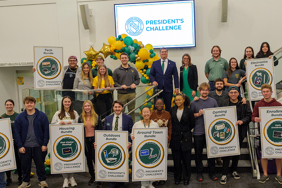A large number of students pose together on a small stage while holding up signs for the prizes they won during the Annual President's Challenge