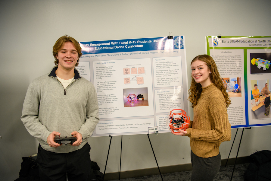 A male and female student stand near a poster presentation.