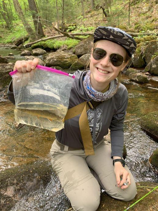Female student in woods with a fish.