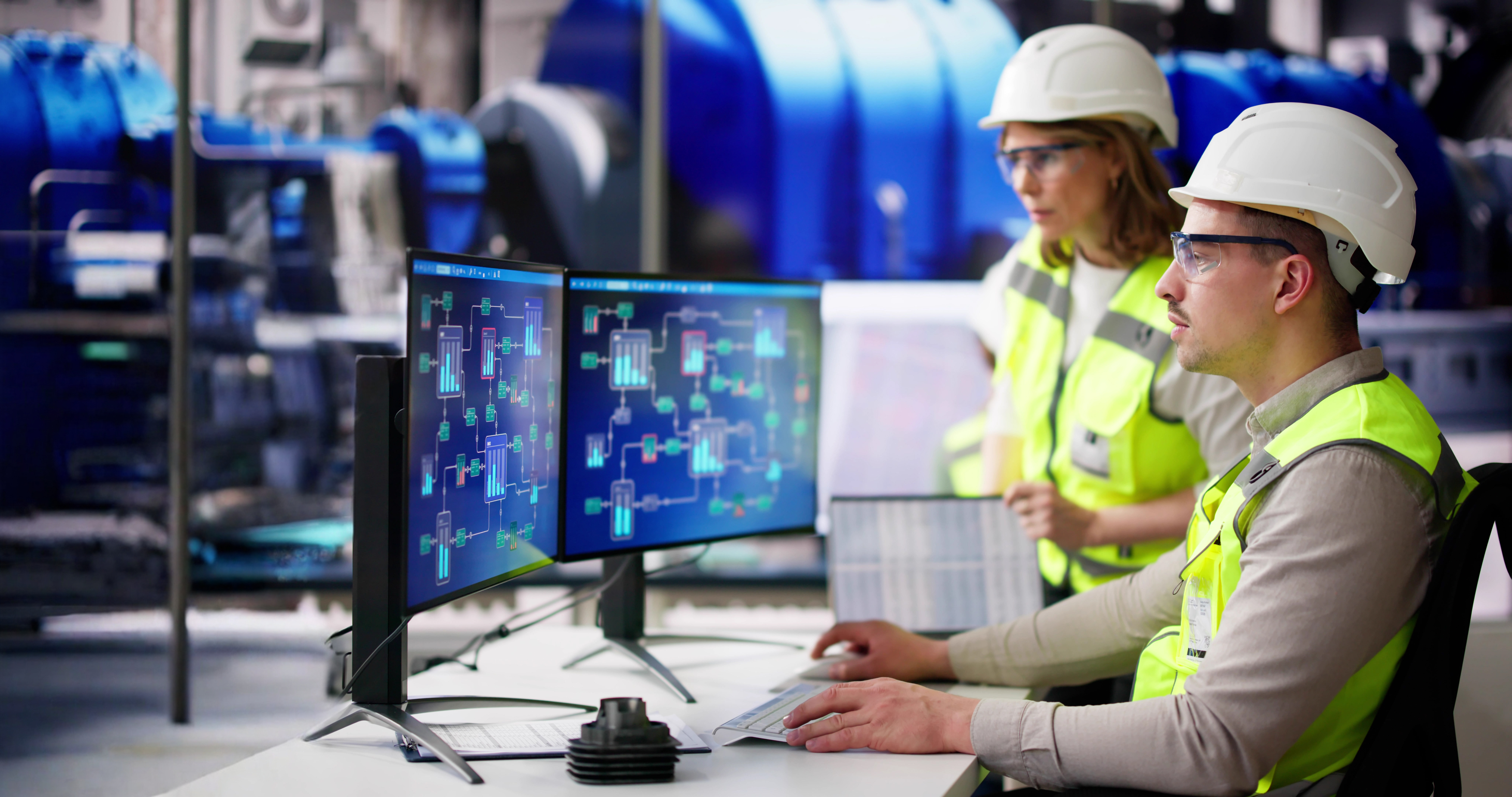 An engineer in a hard hat and high-vis vest sits at a computer displaying grid system technology.