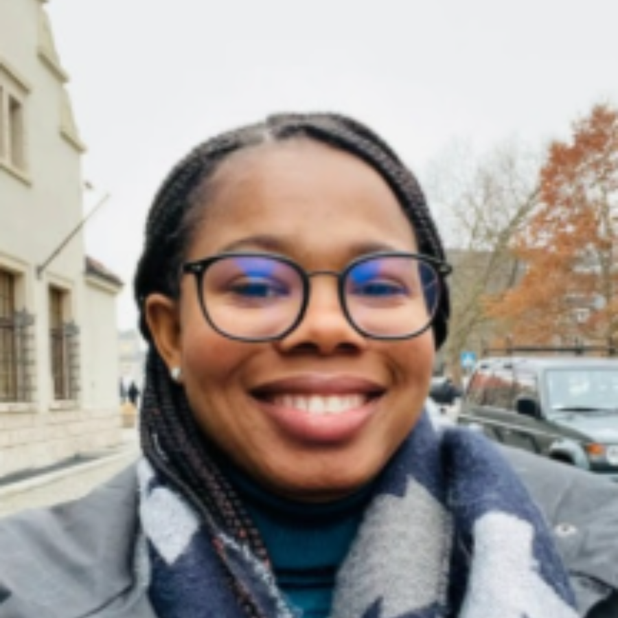 Neka Karen Headshot photo with a building on the left and a tree with orange leaves on the right