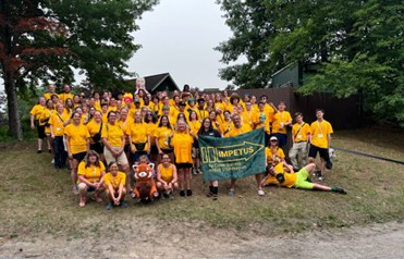 Large group of IMPETUS participants and staff wearing yellow shirts pose outdoors with a banner reading, “IMPETUS for Career Success in NYSED STEM Programs.”
